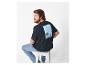 Man in zwart T-shirt met strandprint en jeans, zittend op een kruk.