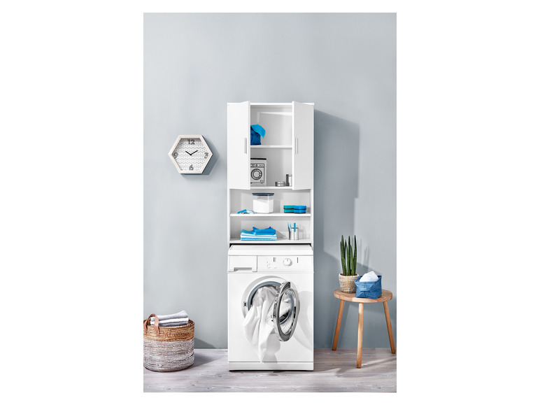 Een wasmachine met een open deur, een wit kastje met planken en een mand met handdoeken