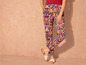 Vrouwelijke broek met kleurrijk patroon en witte sandalen.