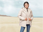 Une femme porte une veste d'hiver beige sur la plage.