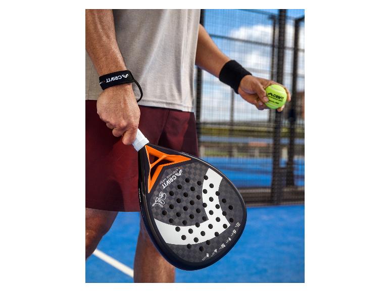 Padelracket en bal vastgehouden door een speler op een padelbaan.