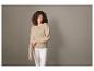 Een vrouw draagt een beige trui en een witte broek.