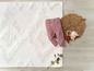 Un pantalon rose pour bébé sur un tapis blanc avec un hochet en bois.