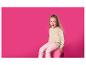 Lachend meisje in beige trui en roze broek zittend op een roze krukje.