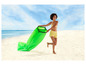 Een vrouw rent met een groene opblaasbare lounge op het strand.
