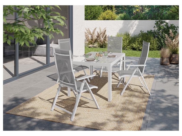 Ensemble de salle à manger extérieur avec table et chaises blanches sur un tapis tressé, entouré de verdure.