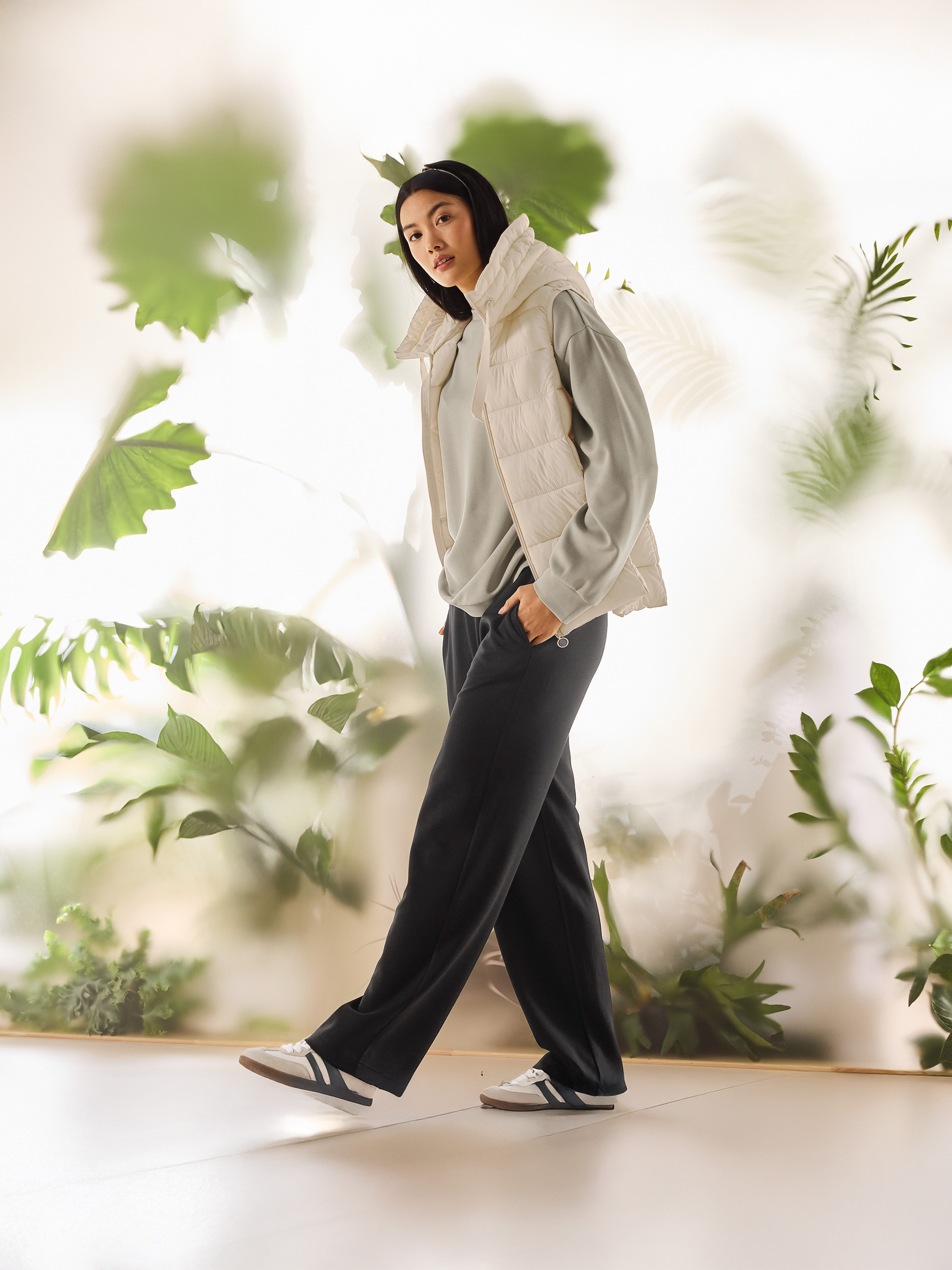 Femme en gilet matelassé beige, sweat-shirt vert clair et pantalon noir marchant.