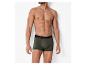 Een man in olijfgroene boxershorts staat tegen een witte muur.