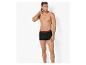 Man in zwarte boxershorts met bordeauxrode tailleband, staand en opzij kijkend.