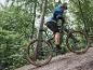 Een man fietst op een grijze elektrische mountainbike met Maxxis banden door een bos.