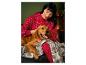 Une femme en pyjama rouge à motifs de flocons de neige câline un chien sur un canapé.