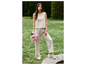Une femme porte un haut et un pantalon beiges avec des baskets blanches dans un jardin vert.