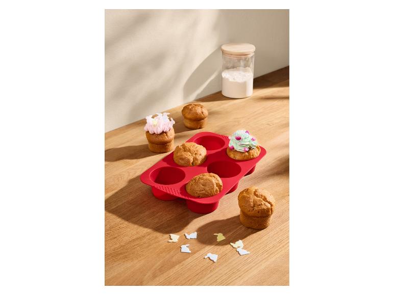 Rode siliconen muffinvorm met muffins, sommige versierd met glazuur.