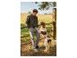 Homme en veste vert olive et pantalon gris avec un chien à la campagne.