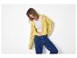 Lachende vrouw in geel opengewerkt vest, witte top en blauwe jeans
