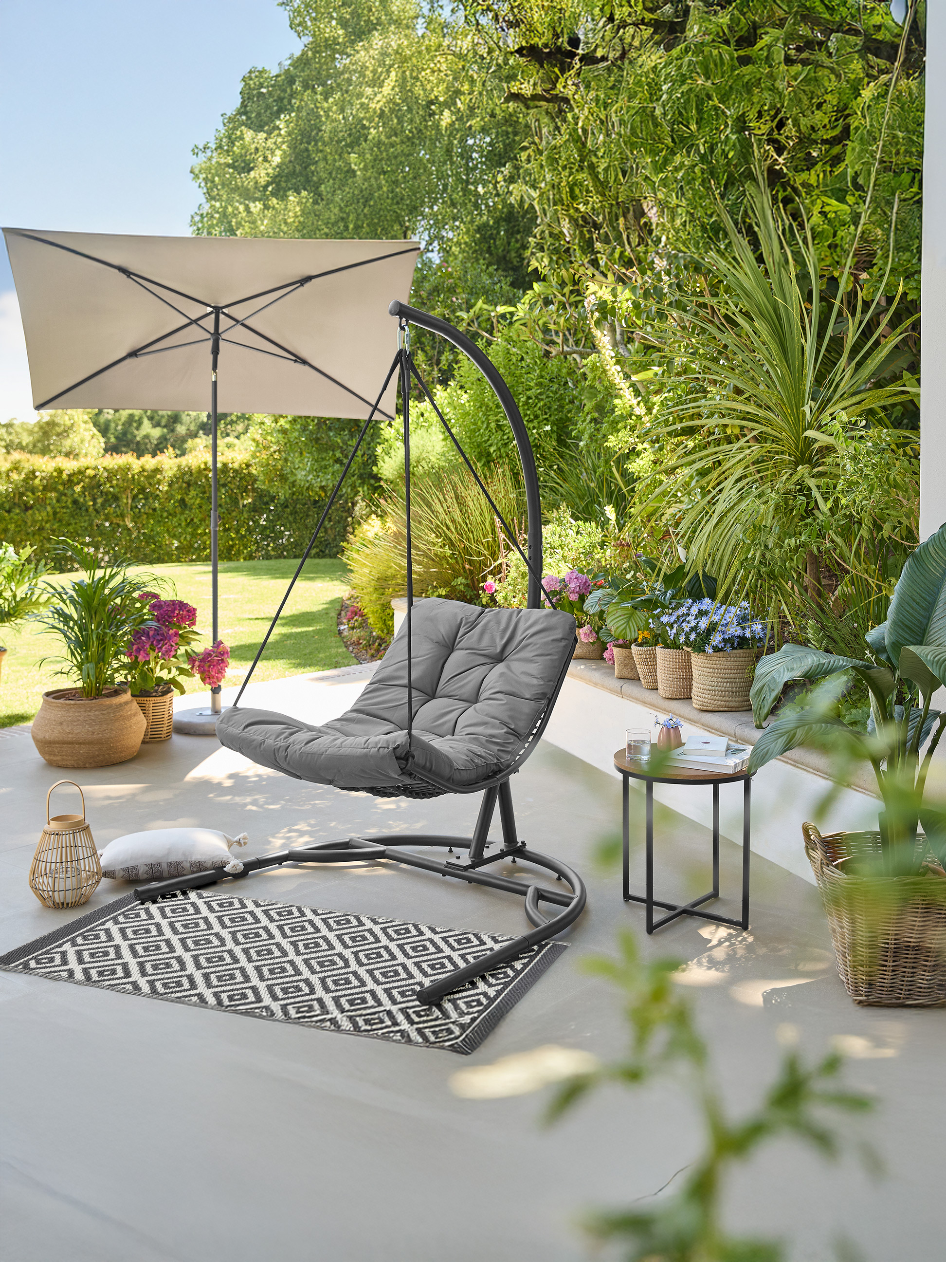 Buiten schommelstoel met grijs kussen, parasol en planten op het terras.