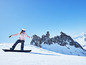 Een snowboarder in roze kleding en blauwe bril, rijdend op een snowboard op een besneeuwde berg