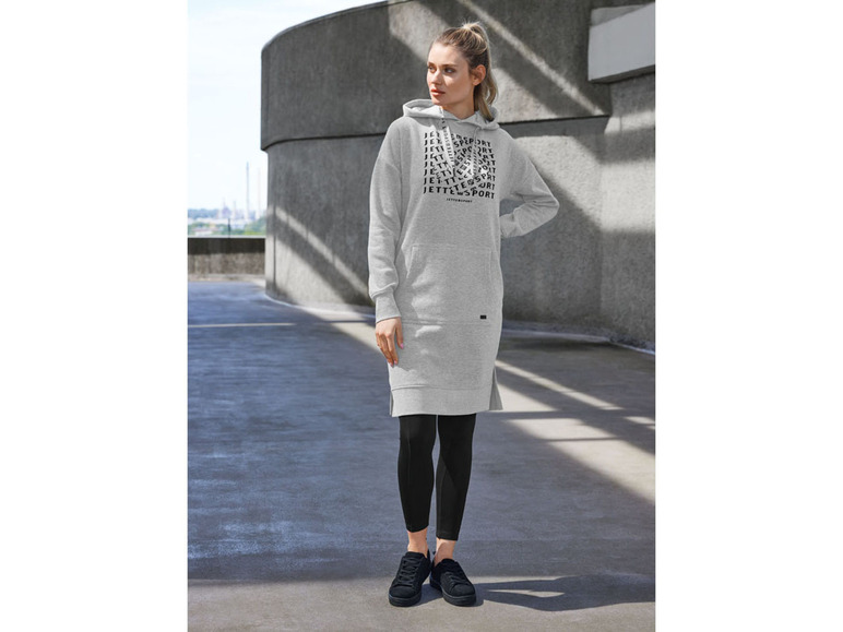 Une femme porte une robe à capuche grise de Jette Joop, un legging noir et des baskets.