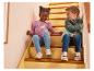 Deux enfants assis dans les escaliers, portant un haut à manches longues violet et une veste verte.