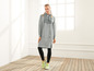 Een vrouw draagt ​​een grijze hoodie-jurk met 'JET's' SPORT-opdruk en zwarte leggings.