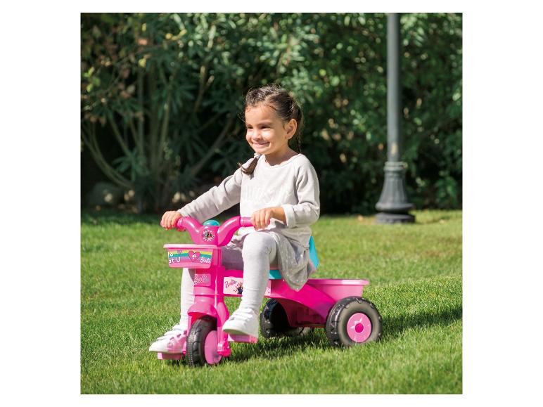 Een meisje rijdt op een roze Barbie driewieler in de tuin.