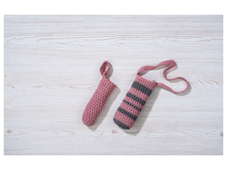 Deux porte-bouteilles en tricot rose, l'un avec une bandoulière, sur une table en bois.