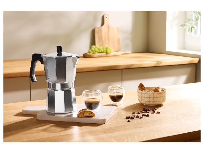 Cafetière moka en aluminium avec deux tasses de café, biscuits et grains de café sur une table en bois.
