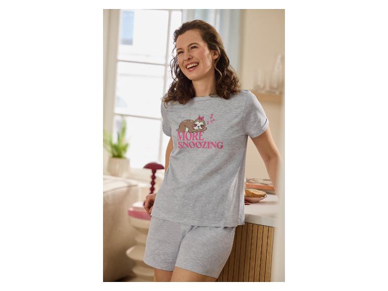 Femme en pyjama gris avec imprimé paresseux et texte 'MORE SNOOZING', souriante dans une pièce lumineuse.