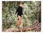 Vrouw in zwarte hoodie en korte broek, sandalen, lopend op een boomstam in een bos.