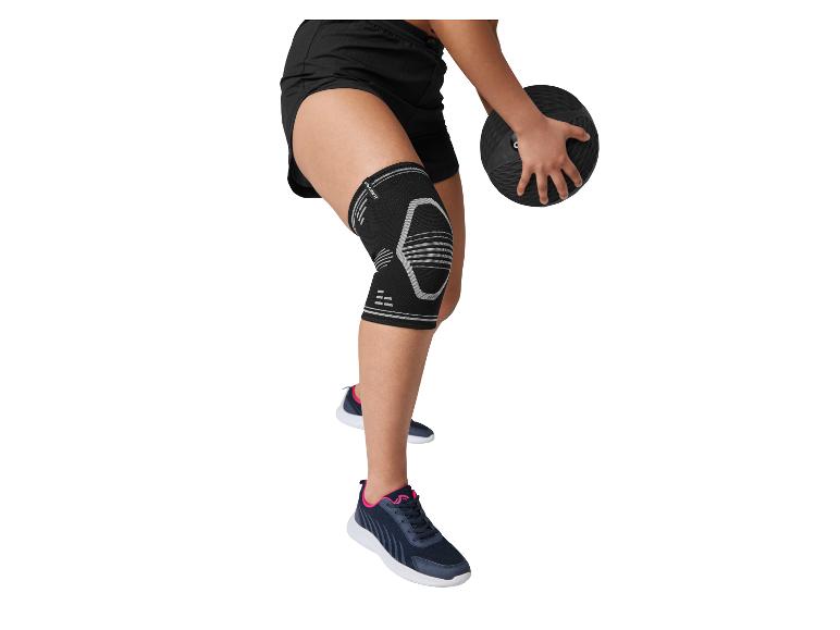 Persoon in zwarte sportshorts, kniebrace en sneakers, met een medicijnbal.