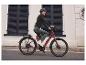 Une femme fait du vélo sur un vélo électrique rouge en ville.