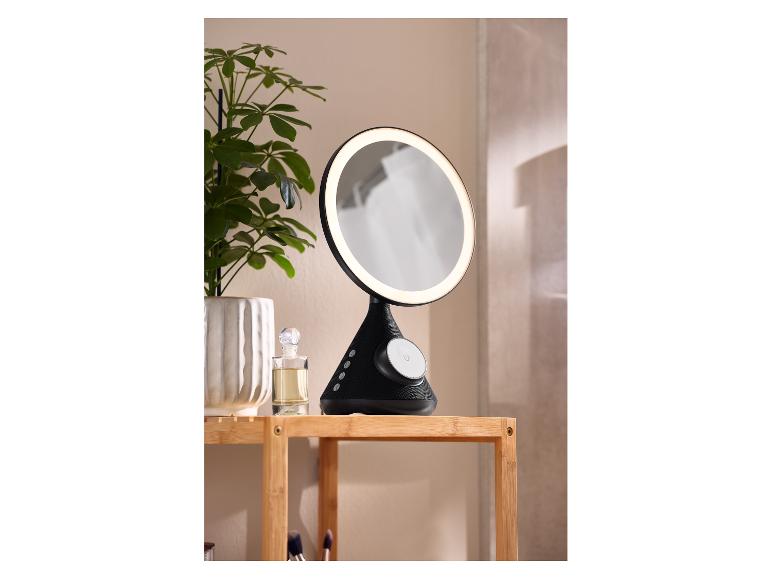 Miroir de maquillage lumineux avec haut-parleur Bluetooth sur étagère en bois avec plante et parfum.