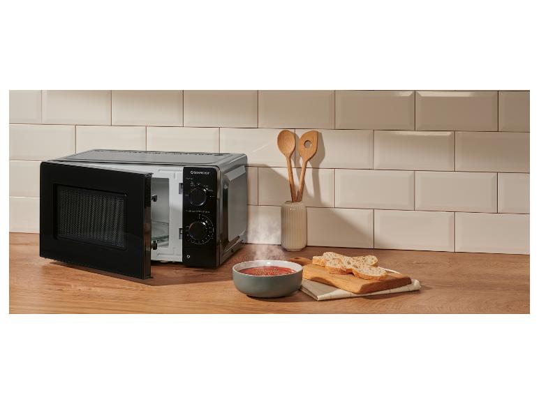 Micro-ondes noir sur un comptoir en bois avec un bol de soupe fumante et du pain.
