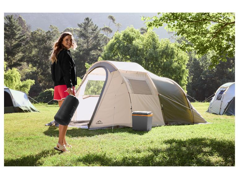 Vrouw met kampeertas en tent op een grasrijke camping.