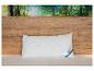 Een wit, gewatteerd kussen met een blauw Beco-label ligt op een bed met houten hoofdeinde en bostapijt.