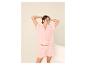 Femme en pyjama rose deux pièces à motif floral, posant les mains derrière la tête.