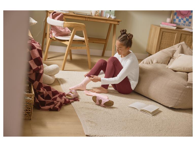 Meisje trekt roze sokken aan op de vloer, met sandalen en een boek.