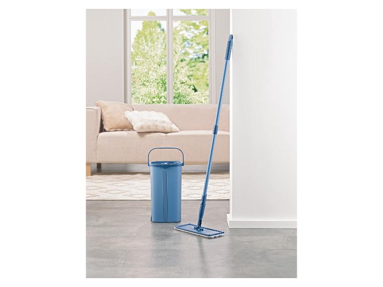 Blauwe emmer en dweil in een lichte woonkamer met bank en raam.