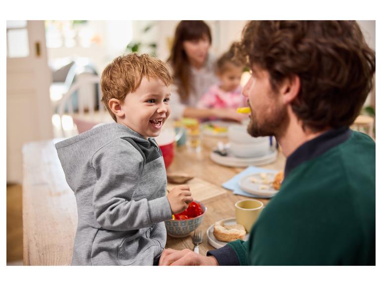 Een jongetje in een grijze hoodie eet aan tafel met zijn familie.
