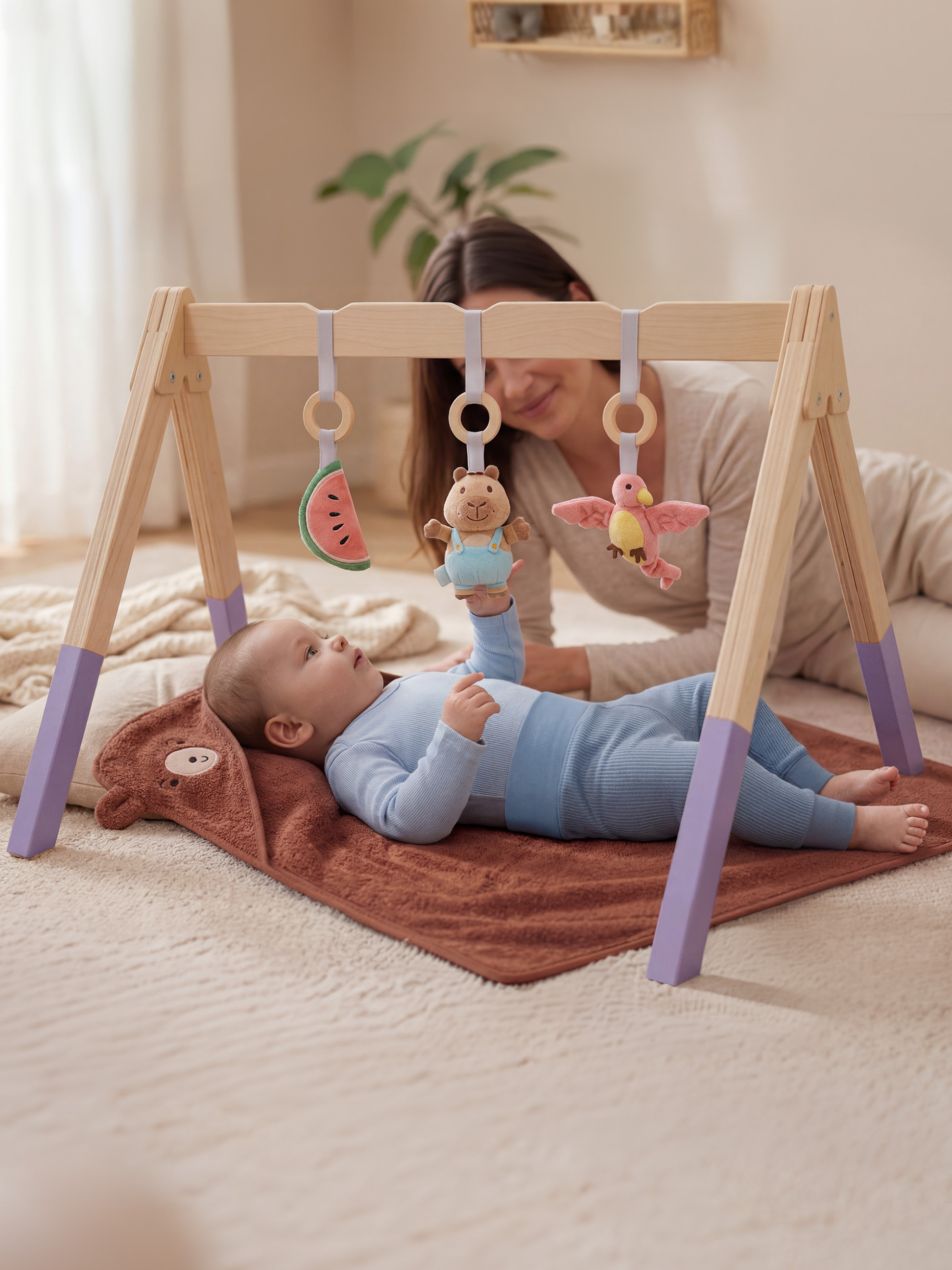 Baby speelt met een houten speelboog met hangend speelgoed, moeder op de achtergrond.