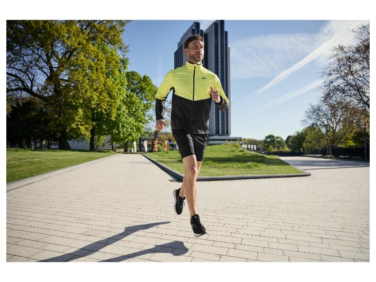 Homme courant dans un parc, portant une veste de course bicolore et un short noir.