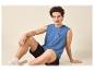 Jonge man in blauw mouwloos shirt met 'SURFING VIBE' opdruk en zwarte korte broek.