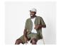 Man in groen overhemd en korte broek, wit T-shirt en pet, zittend op een stoel.