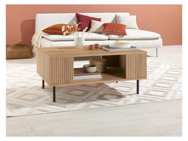 Een lichte houten salontafel met planken, op een licht tapijt voor een lichte bank.