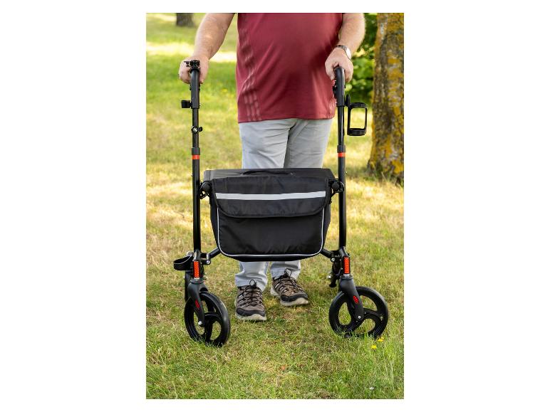 Un homme avec un déambulateur avec un sac et un porte-gobelet dans un champ d'herbe.