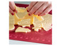 Deeg voor koekjes wordt uitgestoken in verschillende vormen op een rode bakmat.