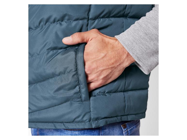 Een man draagt een donkerblauwe gewatteerde vest met zijn hand in de zak.