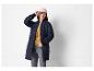 Femme en veste matelassée bleu foncé, cardigan jaune, jean gris et casquette de baseball beige.
