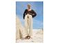 Model draagt een vest, wijde broek en sandalen op het strand.
