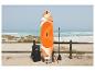 Planche de SUP orange et blanche avec accessoires sur une plage de sable près de la mer.
